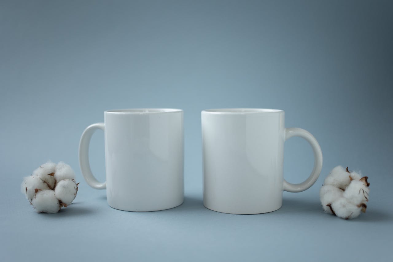 services-img Two white ceramic mugs placed beside cotton flowers on a light blue background, emphasizing minimalism.