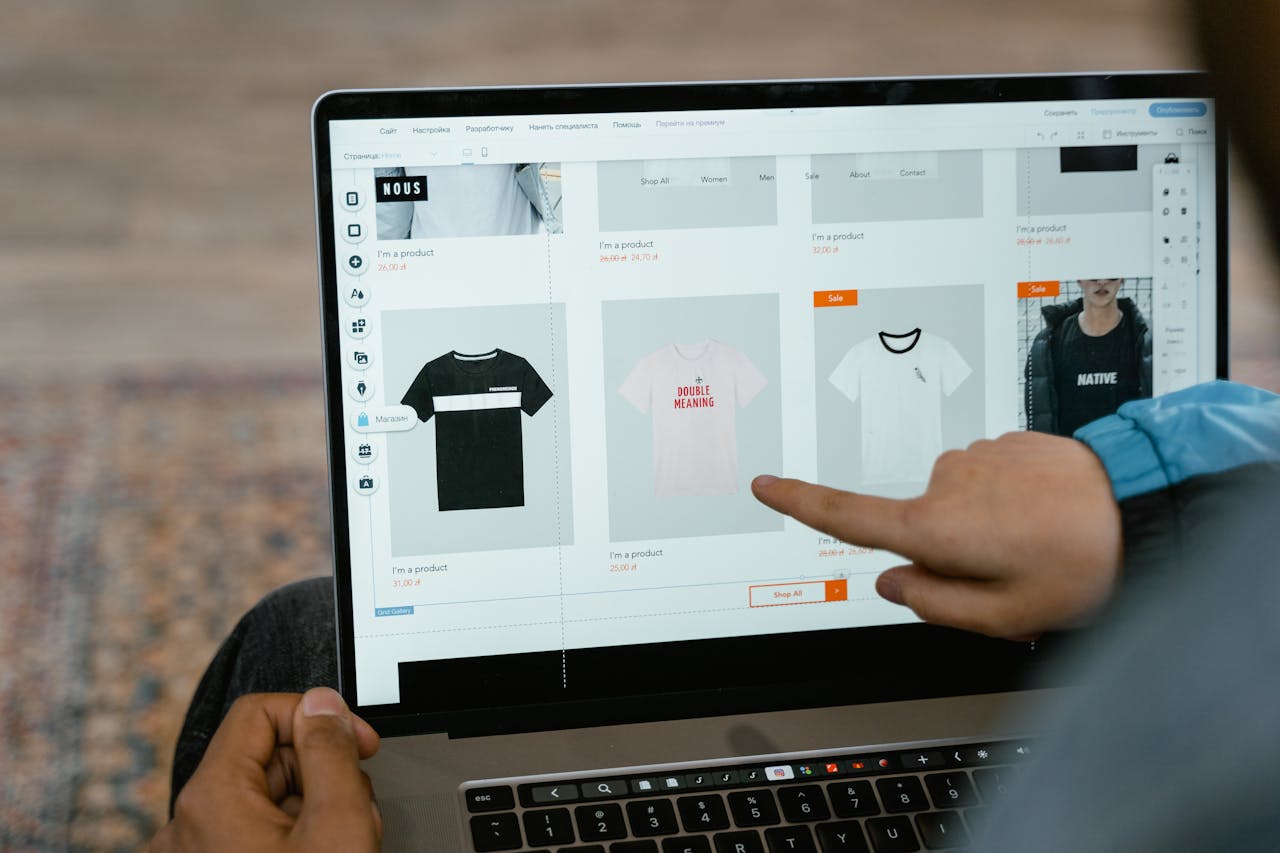 services-02 A person points to t-shirt options in an online store on a laptop screen.